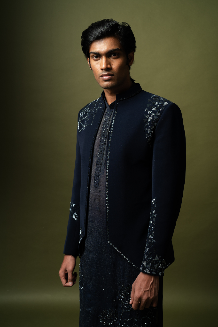 Full-sleeve navy blue Jodhpuri jacket paired with embroidered kurta, worn by a groom on a stool.