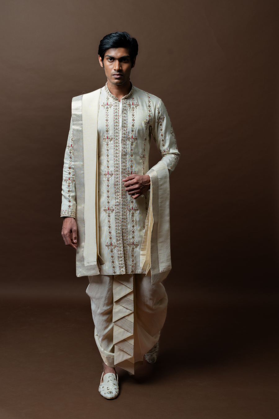 This elegant ivory kurta set, featuring floral thread embroidery and paired with a pleated silk dhoti and matching dupatta, is the perfect ensemble for South Indian grooms.