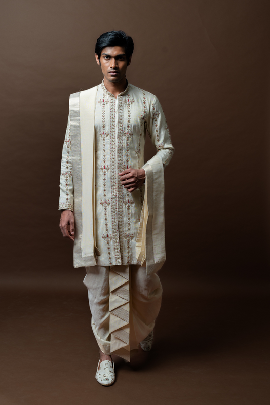This elegant ivory kurta set, featuring floral thread embroidery and paired with a pleated silk dhoti and matching dupatta, is the perfect ensemble for South Indian grooms.