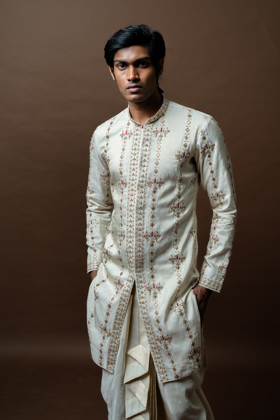 A graceful ivory kurta adorned with thread embroidery, complemented by a pleated silk dhoti and matching stole. Designed for South Indian ceremonies and receptions.