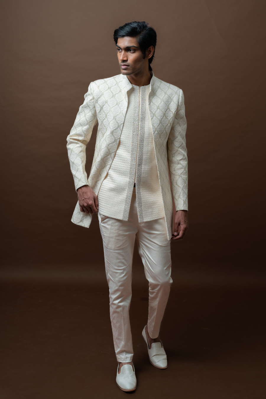 Man standing in regal ivory sherwani-inspired Jodhpuri suit, styled for elegant wedding functions.