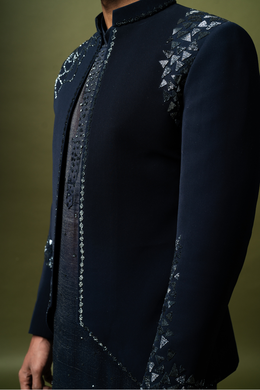 Male model in navy Jodhpuri suit with refined detailing, sitting in a relaxed pose for wedding fashion campaign.