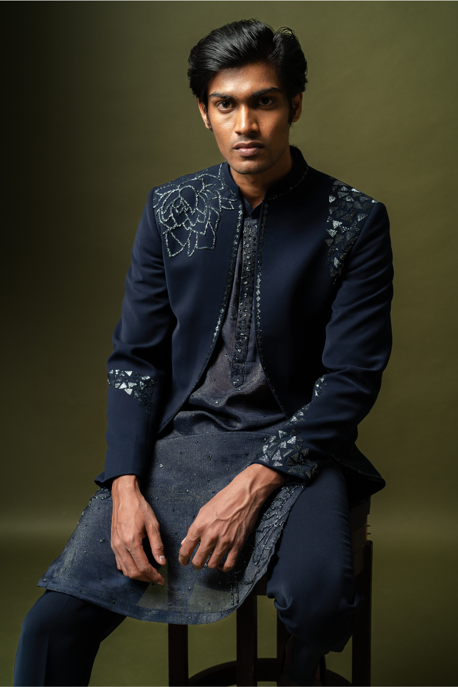 Man seated in a navy blue embroidered Jodhpuri suit, ideal for weddings and formal ethnic events.