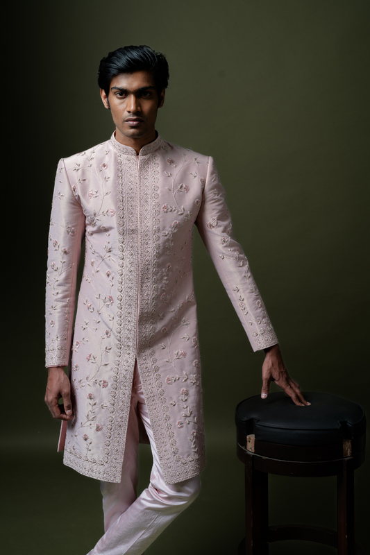 Man standing in an elegant blush pink sherwani with intricate embroidery, ideal for South Indian wedding rituals.

