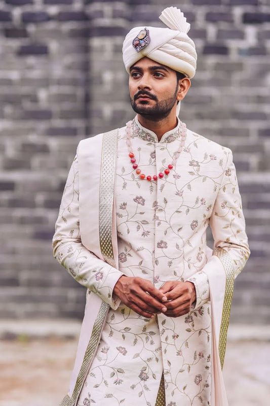 South Indian groom wearing ivory floral hand-embroidered Pattu Sherwani with gold border dupatta, turban, and coral bead mala, ideal for wedding, Muhurtham, and Pellikoduku ceremonies in Hyderabad.